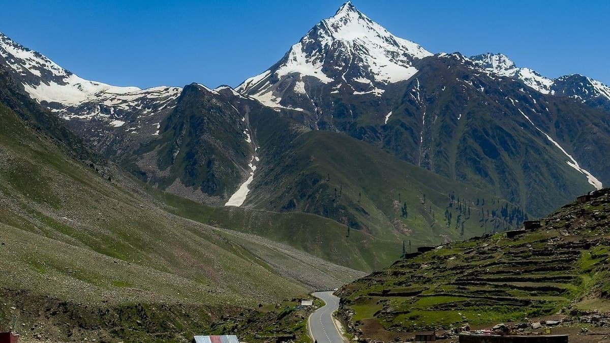 The road to the Babusar Pass climbing through green slopes towards a snow-covered peak