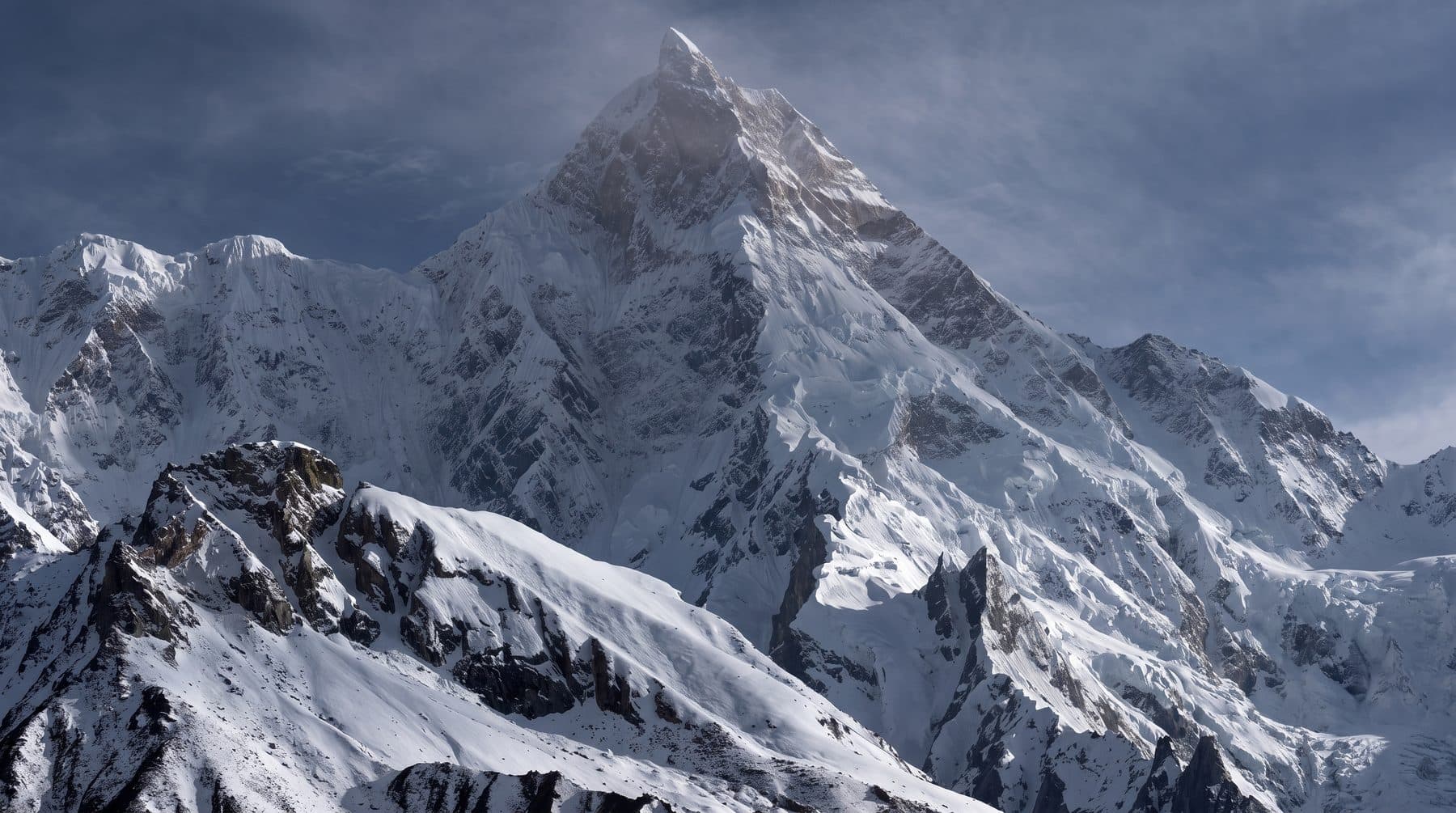 Masherbrum's summit pyramid and snow face under a windswept sky