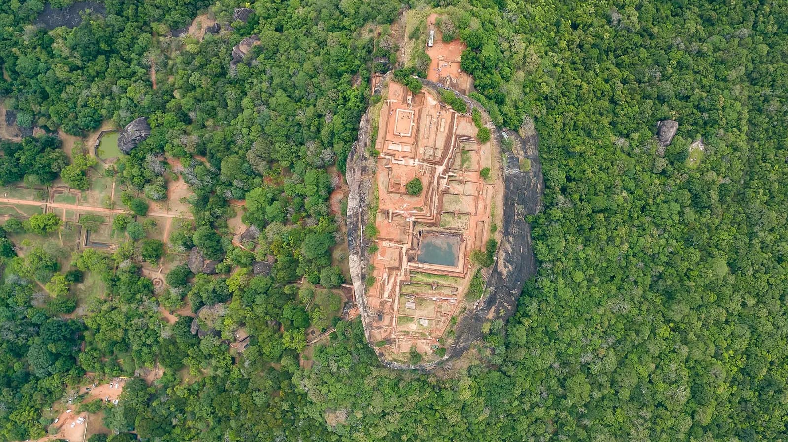 Aerial view straight down on Sigiriya rock, its flat summit covered in the brick foundations of the palace and a rock-cut pool, surrounded by forest