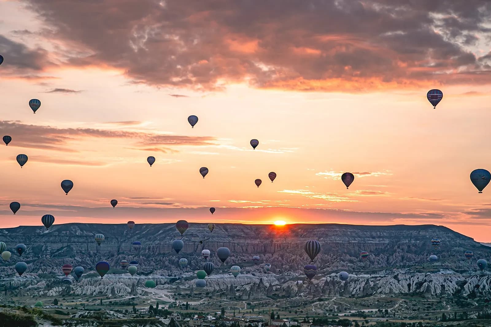 Dozens of hot air balloons rising at sunrise over the eroded valleys and rock cones around Göreme in Cappadocia