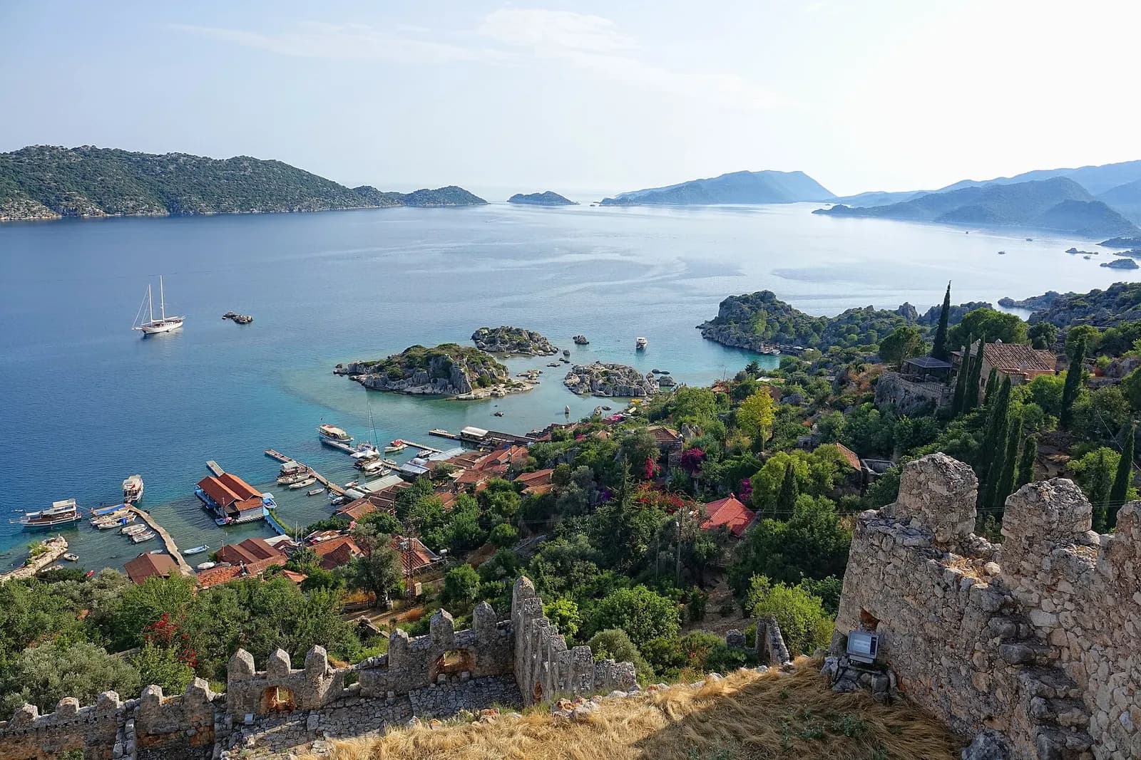 View from the walls of Simena castle over the red roofs and jetties of Kaleköy to Kekova island, with a two-masted gulet anchored in the bay