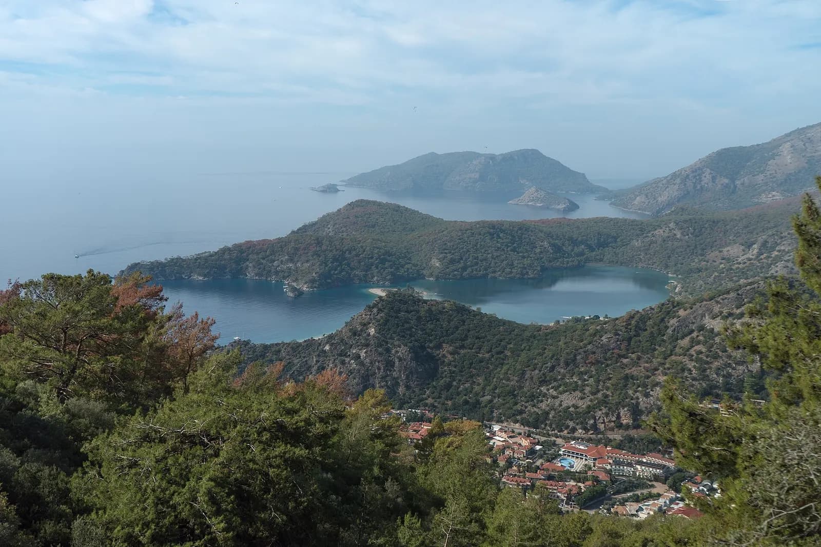 View from the Lycian Way down through pine forest to the Blue Lagoon at Ölüdeniz, with wooded headlands and islands in a hazy sea