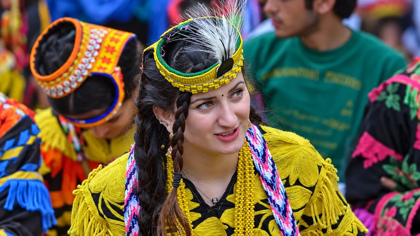 A young Kalasha woman with braided hair celebrating a cultural festival in Chitral, wearing a bright yellow dress, beaded necklaces, and a traditional headdress adorned with cowrie shells and a white feather.
