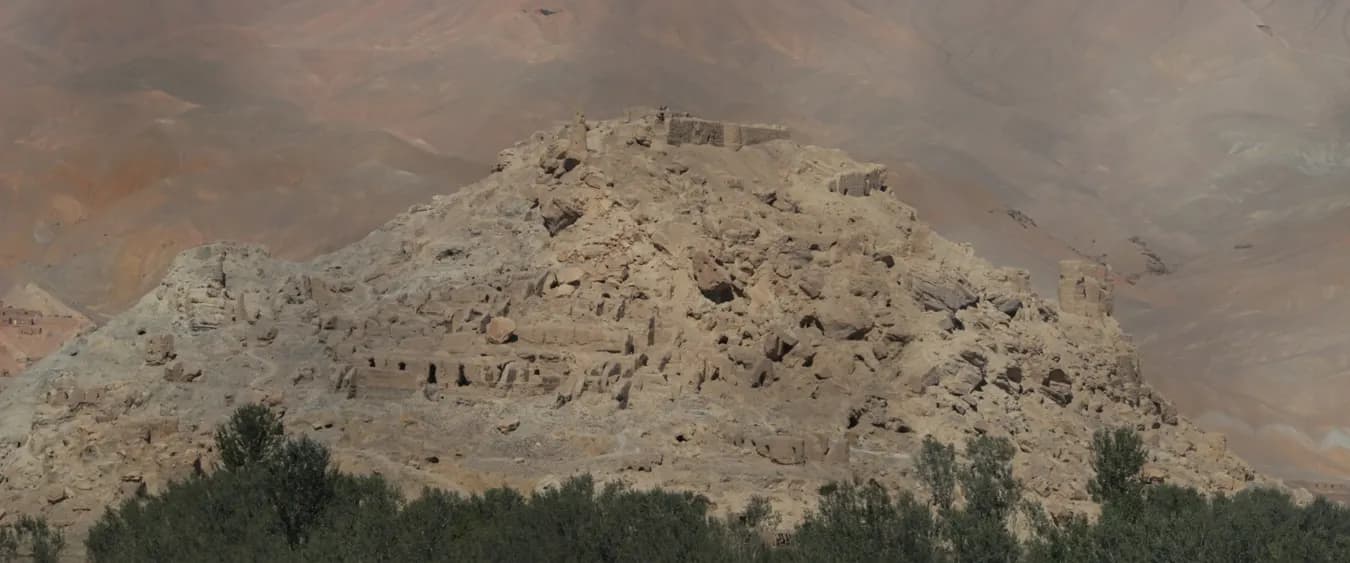 The crumbling mud-brick ruins of Shahr-e Gholghola on a hilltop in the Bamiyan valley, with trees in the foreground and bare hills behind