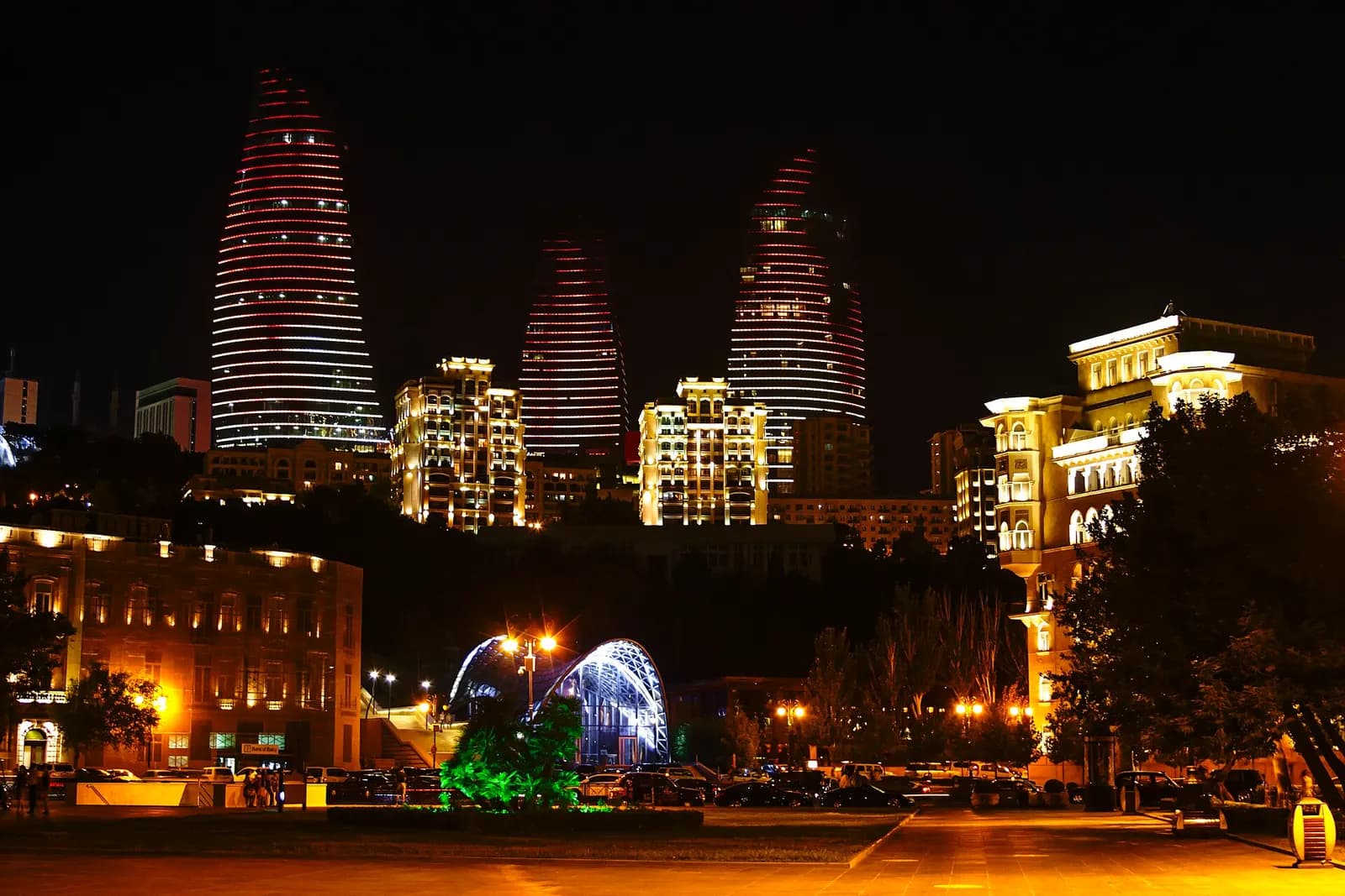 The three Flame Towers lit red and white at night on the hill above Baku, with the funicular station and seafront buildings below
