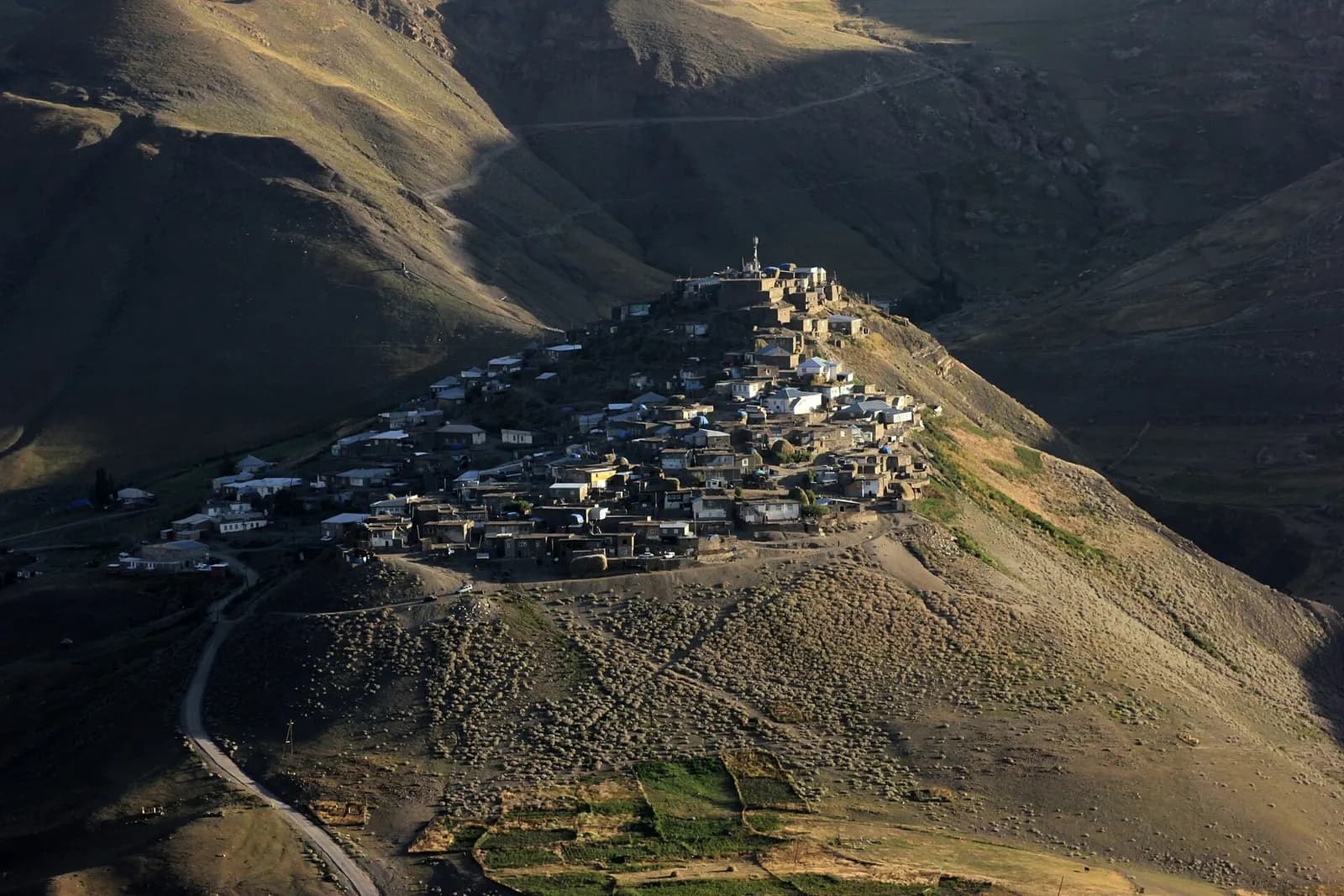 The stone houses of Khinaliq village stacked on a ridge in the Greater Caucasus, with bare mountain slopes and a winding road below