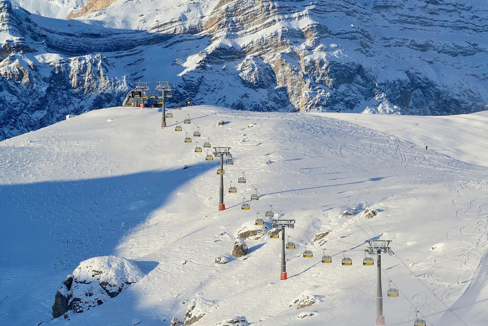 A chairlift climbing a snow-covered slope at Shahdag Mountain Resort beneath limestone cliffs in the Greater Caucasus