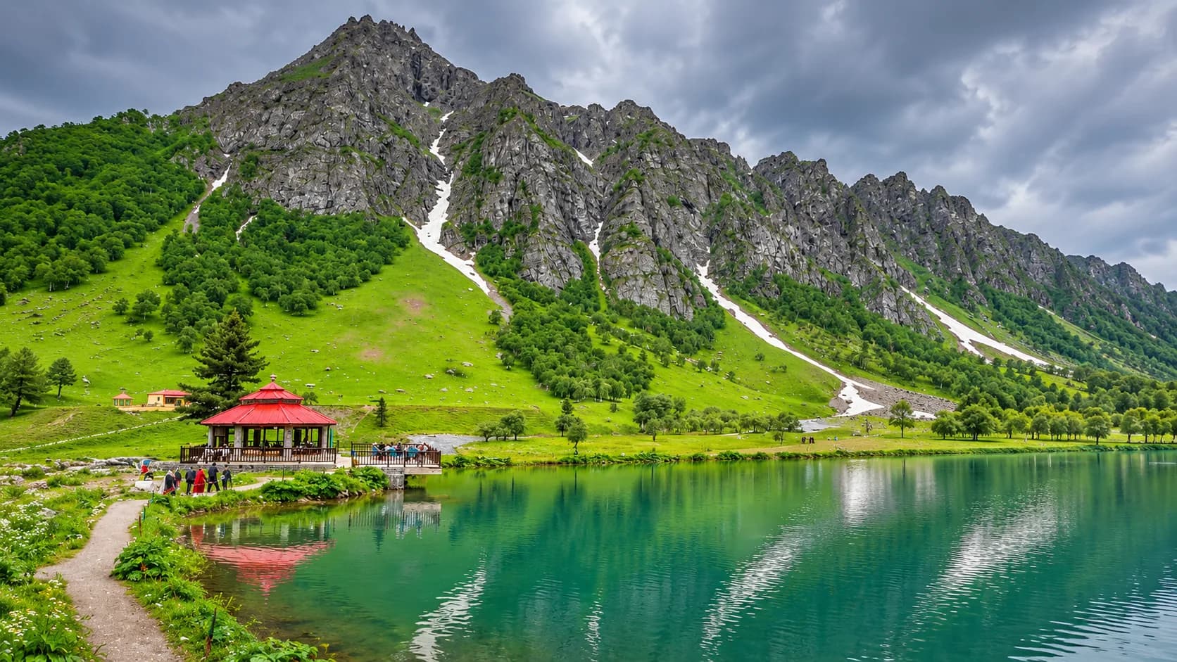 A red-roofed wooden gazebo pavilion perched on the edge of an emerald-green alpine lake in Naltar Valley, surrounded by verdant meadows, pine forests, and a sheer, rocky mountain ridge with snow couloirs.